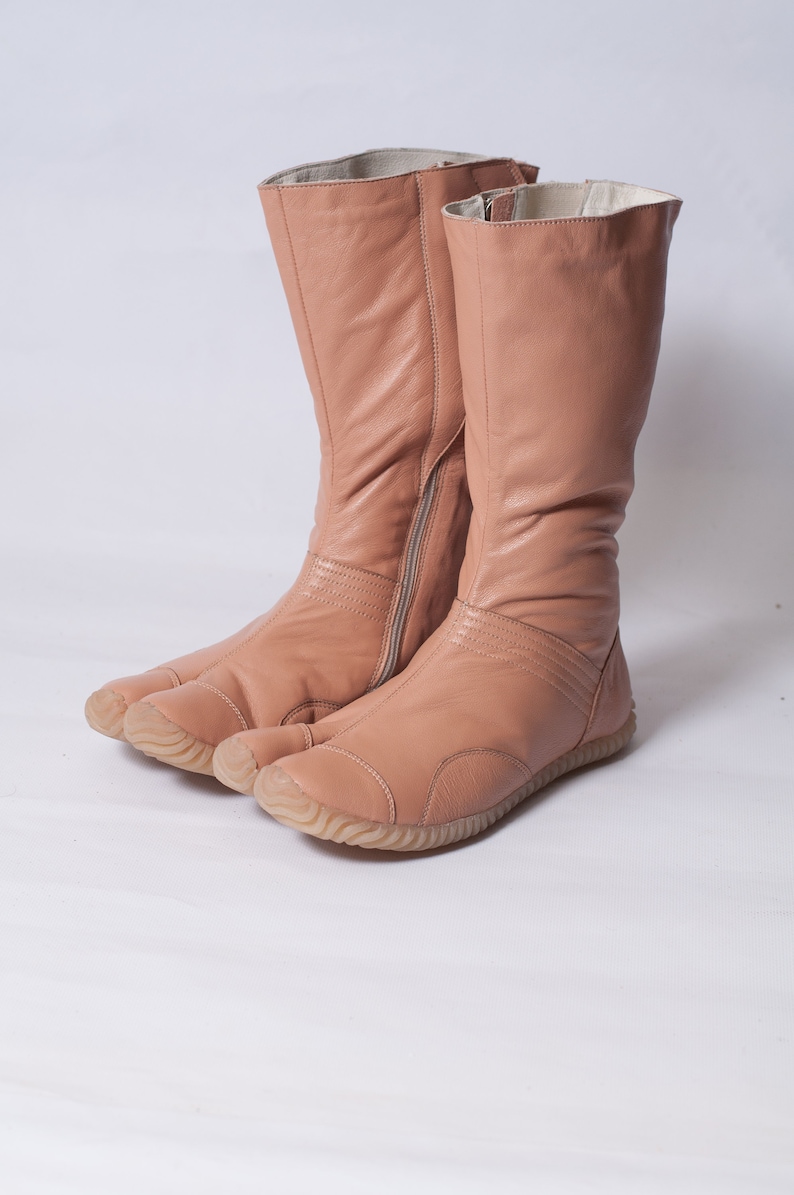 Puede incluir: Un par de botas de cuero marr&oacute;n claro con un dise&ntilde;o &uacute;nico de punta dividida. Las botas tienen una cremallera en el interior de cada bota y una suela de goma.