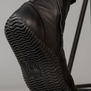 May include: Black leather ankle boots with a zipper up the back and a textured rubber sole. The sole has the word "Vibram" printed on it.
