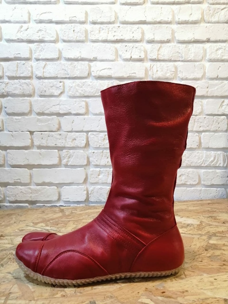 Pu&ograve; includere: Stivali in pelle rossa con un design a punta divisa. Gli stivali hanno una suola spessa e un gambale alto.