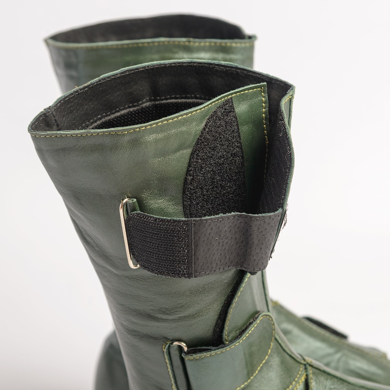 Puede incluir: Un par de botas de cuero verde con correas y hebillas negras. Las botas tienen una cremallera en el lateral y una punta puntiaguda.