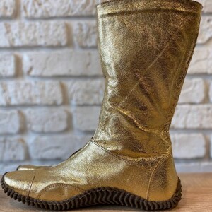 May include: Gold leather boots with a textured sole. The boots are knee-high and have a pointed toe.