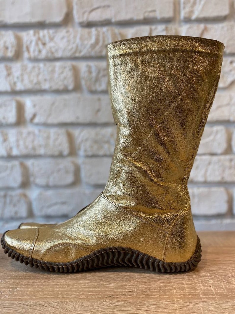 May include: Gold leather boots with a textured sole. The boots are knee-high and have a pointed toe.