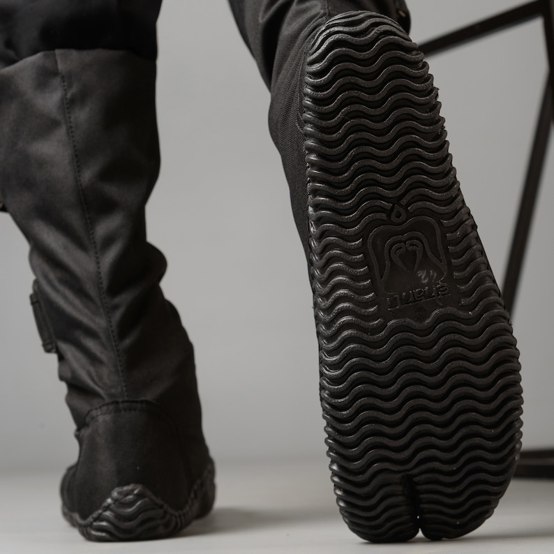 May include: Black tabi boots with a textured sole and the word "TABI" printed on the sole.