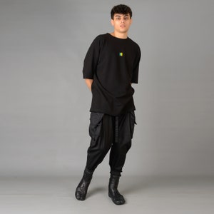 May include: A person wearing a black oversized t-shirt with a small colorful graphic on the front, black cargo pants, and black boots.