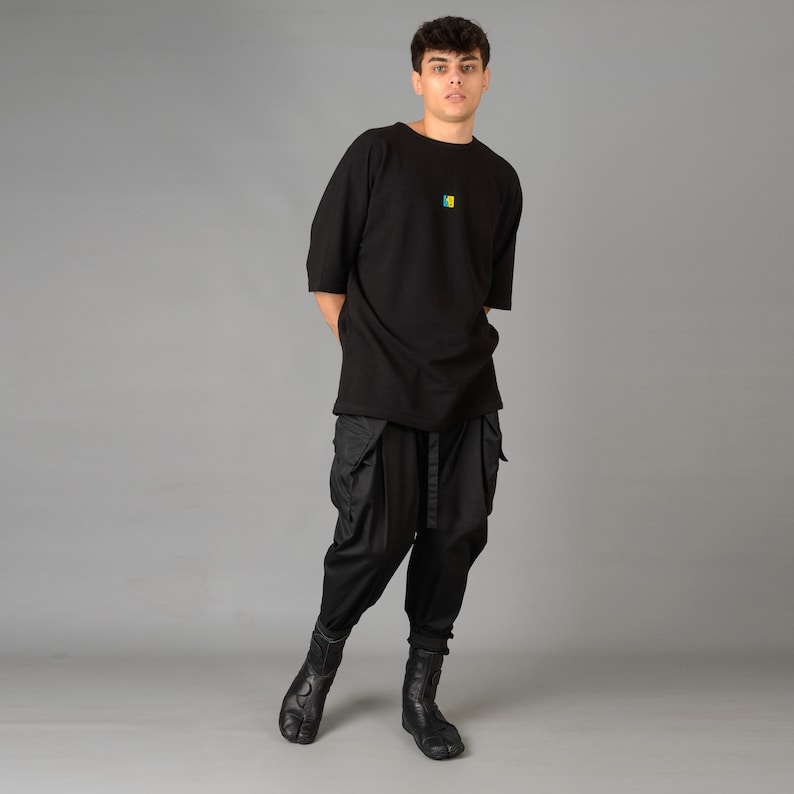 May include: A person wearing a black oversized t-shirt with a small colorful graphic on the front, black cargo pants, and black boots.