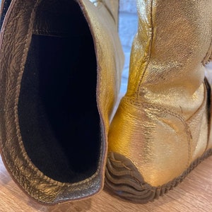 May include: A pair of gold leather boots with a black lining. The boots have a textured sole and are made of a soft, supple leather.