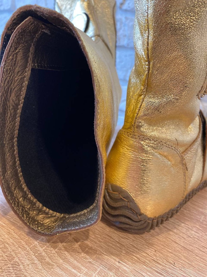 May include: A pair of gold leather boots with a black lining. The boots have a textured sole and are made of a soft, supple leather.