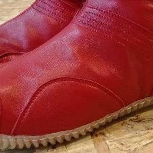 Pu&ograve; includere: Stivali tabi in pelle rossa con suola in gomma testurizzata. Gli stivali hanno una punta a punta e una cerniera sul retro.