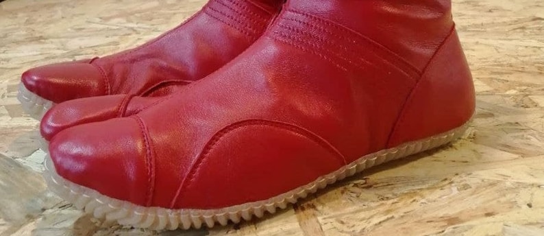 Pu&ograve; includere: Stivali tabi in pelle rossa con suola in gomma testurizzata. Gli stivali hanno una punta a punta e una cerniera sul retro.