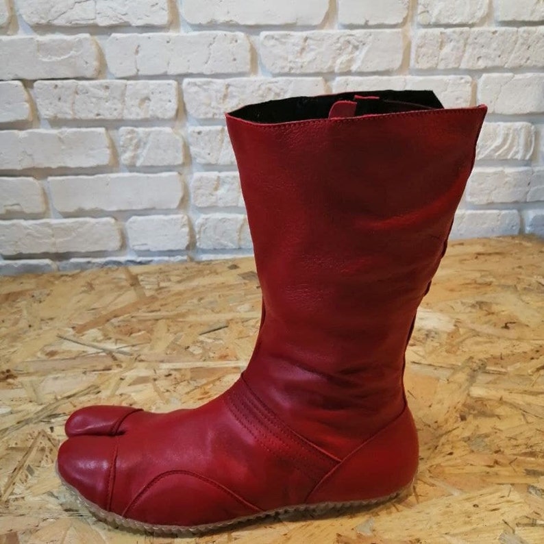 Pu&ograve; includere: Stivali in pelle rossa con un design a punta divisa. Gli stivali hanno un gambale alto e una cerniera sul retro.