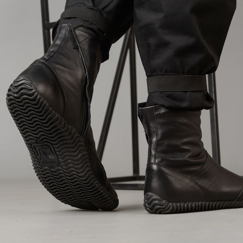 May include: Black leather ankle boots with a zipper on the side and a textured rubber sole. The boots have a strap around the ankle.