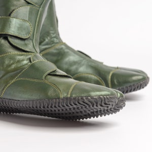 Puede incluir: Un par de botas de cuero verde con un dise&ntilde;o &uacute;nico de punta dividida. Las botas tienen una suela de goma texturizada y una correa en la parte superior.