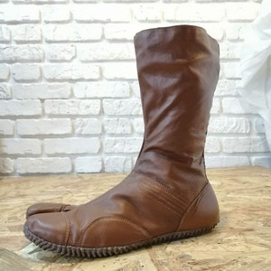 Puede incluir: Botas de cuero marr&oacute;n con un dise&ntilde;o de punta dividida. Las botas tienen un eje alto y un estilo simple y minimalista.