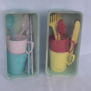 May include: Two vintage plastic children's dining sets in clear plastic containers. One set is pink and teal, the other is red and yellow. Each set includes a cup, spoon, fork, knife, and chopsticks.