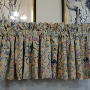 May include: A gathered window valance featuring a cream-colored fabric with a repeating floral and vine pattern in shades of blue, pink, and muted orange. The valance is suspended on a black rod and displays a ruffled top header with pleats.