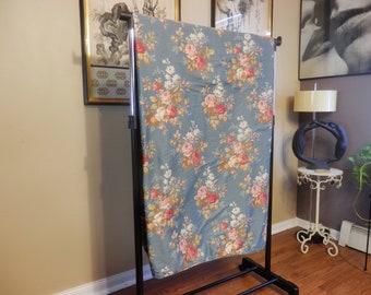 Puede incluir: Una tela floral azul con un patrón floral rosa, blanco y amarillo. La tela está colgada en un soporte de metal negro.