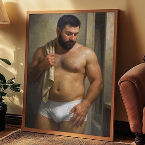 Puede incluir: Una impresión enmarcada de un hombre en ropa interior blanca, sosteniendo una toalla. La obra de arte está apoyada contra una pared. La habitación tiene una paleta de colores cálidos, con una alfombra estampada y una planta en maceta.