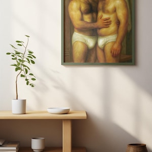 Puede incluir: Pintura enmarcada que representa a dos hombres en calzoncillos blancos abraz&aacute;ndose. La obra de arte, con un marco verde, se exhibe en una pared blanca. Una estanter&iacute;a de madera debajo contiene una peque&ntilde;a planta, un cuenco y una taza, con una cesta de mimbre en el suelo.
