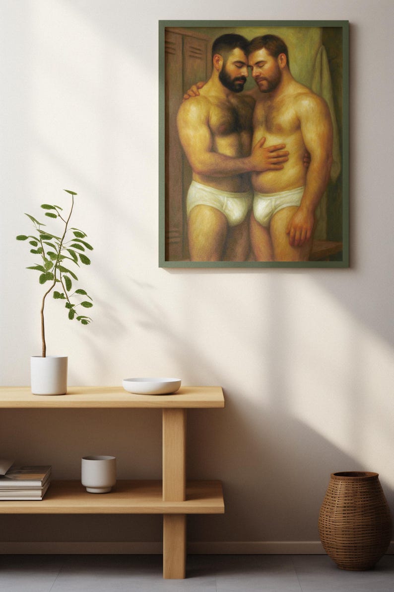 Puede incluir: Pintura enmarcada que representa a dos hombres en calzoncillos blancos abraz&aacute;ndose. La obra de arte, con un marco verde, se exhibe en una pared blanca. Una estanter&iacute;a de madera debajo contiene una peque&ntilde;a planta, un cuenco y una taza, con una cesta de mimbre en el suelo.