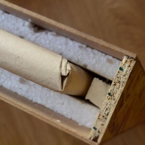 Puede incluir: Un tubo de cart&oacute;n marr&oacute;n envuelto en papel marr&oacute;n se coloca dentro de una caja de madera con cacahuetes de embalaje blancos. La caja est&aacute; hecha de madera contrachapada y tiene un acabado de madera natural.