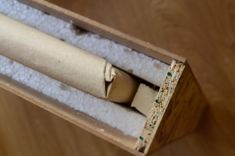 Puede incluir: Un tubo de cart&oacute;n marr&oacute;n envuelto en papel marr&oacute;n se coloca dentro de una caja de madera con cacahuetes de embalaje blancos. La caja est&aacute; hecha de madera contrachapada y tiene un acabado de madera natural.