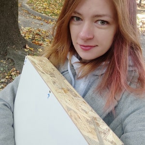 Pu&ograve; includere: Un pannello di tela bianca con una cornice in legno. Il pannello &egrave; tenuto da una persona con lunghi capelli rossi. Il pannello ha delle frecce blu disegnate su di esso.