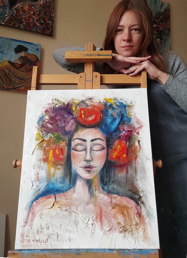 Pu&ograve; includere: Un dipinto di una donna con gli occhi chiusi, che indossa una corona di fiori colorati. Il dipinto &egrave; su una tela bianca con una superficie strutturata. Il viso della donna &egrave; dipinto in uno stile realistico, con tratti delicati e un'espressione serena. La corona &egrave; composta da fiori rossi, blu e viola brillanti. Lo sfondo del dipinto &egrave; di colore azzurro chiaro.