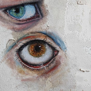 Puede incluir: Primer plano de dos ojos pintados en una pared blanca texturizada. El ojo superior es azul con un iris verde y el ojo inferior es marr&oacute;n con un iris marr&oacute;n oscuro. La firma del artista "Kushnir I. 2022" es visible en la esquina inferior derecha.