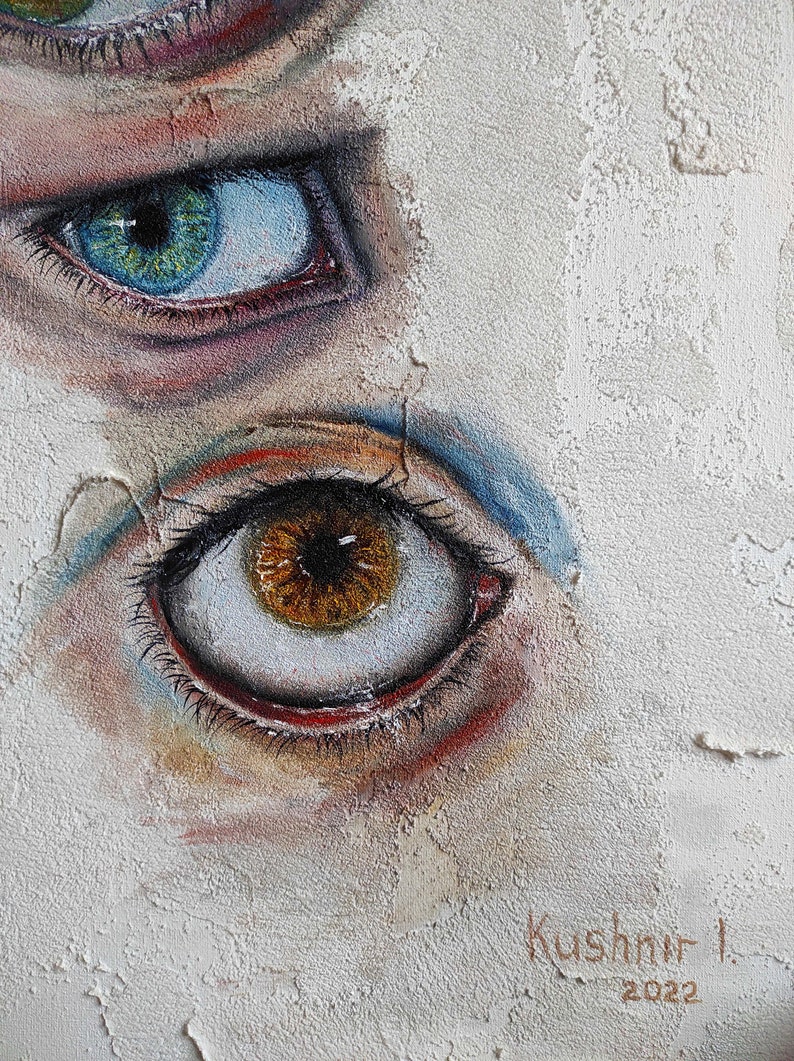 Puede incluir: Primer plano de dos ojos pintados en una pared blanca texturizada. El ojo superior es azul con un iris verde y el ojo inferior es marr&oacute;n con un iris marr&oacute;n oscuro. La firma del artista "Kushnir I. 2022" es visible en la esquina inferior derecha.