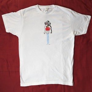 May include: White t-shirt with a black and white illustration of a person with a red heart and blue legs. The text "Phil Bug" is printed below the illustration.