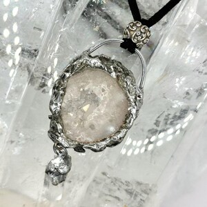 May include: A silver pendant necklace featuring a clear quartz crystal set in a silver frame. The pendant hangs from a black cord.