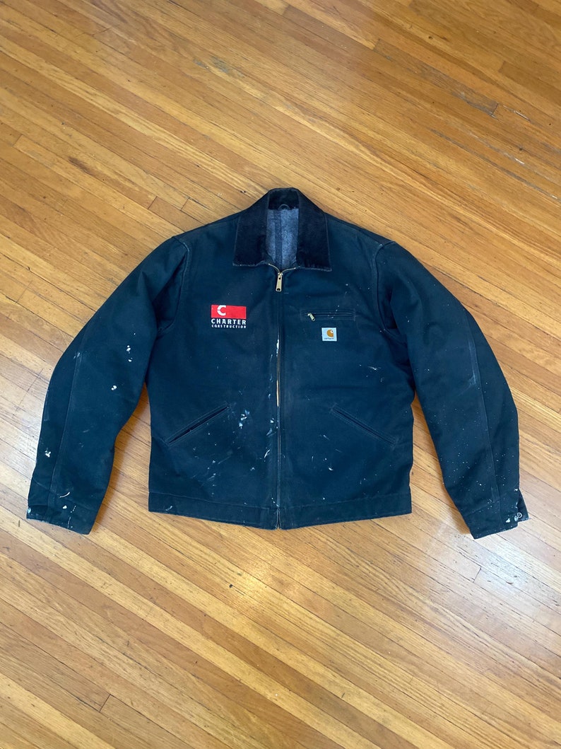 May include: A black Carhartt work jacket with a red and white logo that says "Charter Communications" on the left chest. The jacket has a corduroy collar and is covered in white paint splatters.