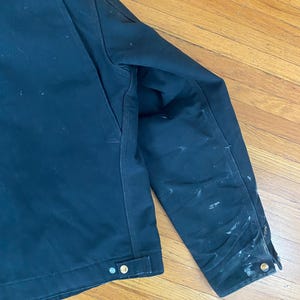 May include: A dark blue work jacket with a zip closure and multiple pockets. The jacket has a worn look with visible dirt and wear marks.