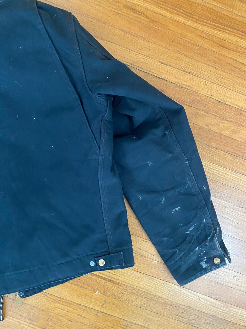 May include: A dark blue work jacket with a zip closure and multiple pockets. The jacket has a worn look with visible dirt and wear marks.