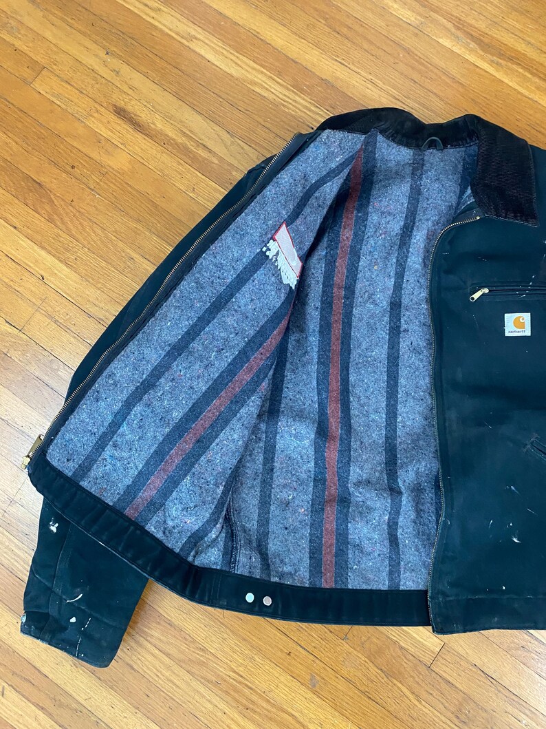 May include: A black Carhartt work jacket with a striped flannel lining. The jacket has a zip closure and a corduroy collar.