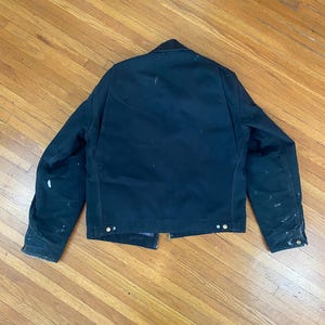May include: A dark blue work jacket with a zip closure and multiple pockets. The jacket has a worn look with white paint splatters on the fabric.