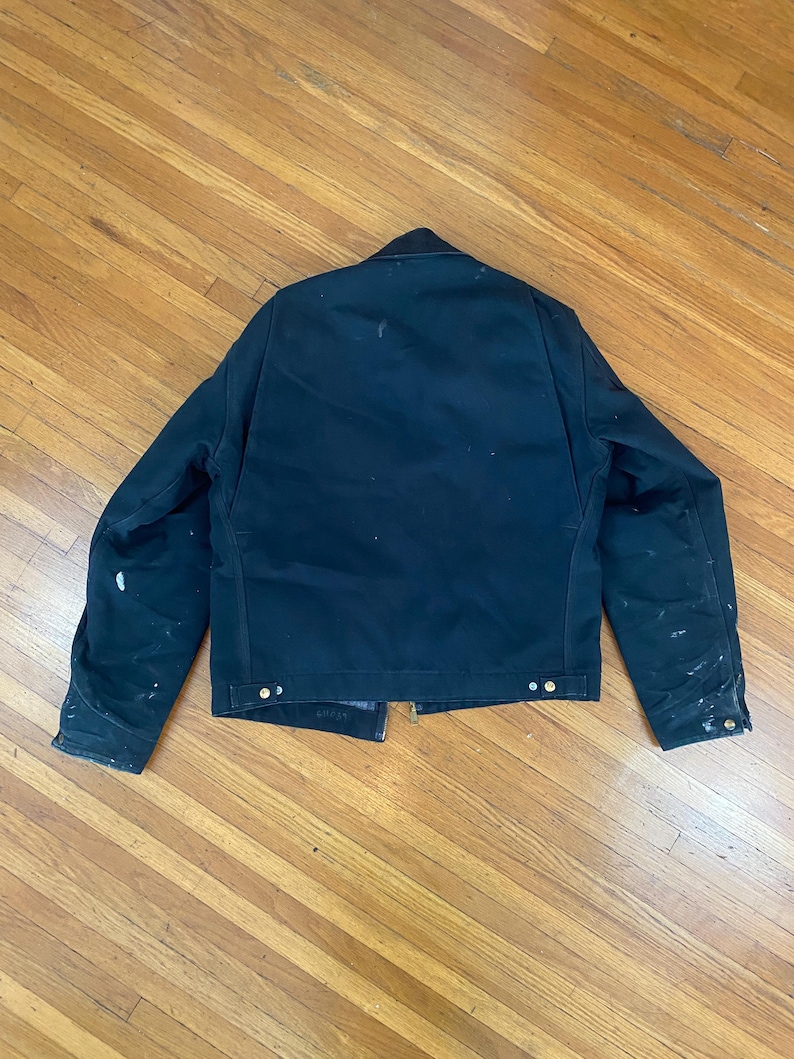 May include: A dark blue work jacket with a zip closure and multiple pockets. The jacket has a worn look with white paint splatters on the fabric.