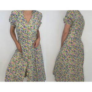 May include: A floral print midi dress with a button-up front and short puff sleeves. The dress is a light green base with pink, yellow, and purple flowers.