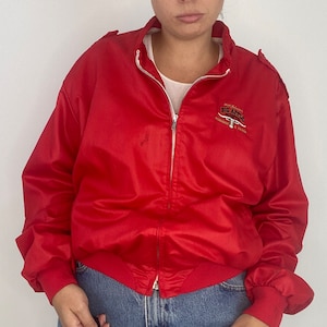 May include: Red satin bomber jacket with a zipper closure and a Big Apple logo embroidered on the front. The logo features a steer head and the text "Big Apple Western Wear, Hollywood, CA".