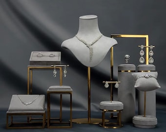 May include: A set of jewelry display stands with a gray velvet finish and gold accents. The stands feature a variety of shapes and sizes, including a bust form, a ring stand, and a bracelet stand. The stands are perfect for displaying jewelry in a retail setting.