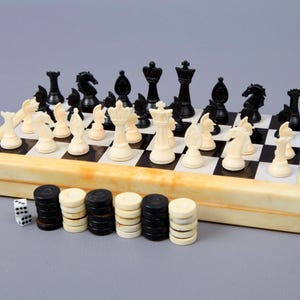 Puede incluir: Un juego de ajedrez y damas de viaje vintage con un tablero de madera, piezas de ajedrez blancas y negras y damas blancas y negras. El juego incluye un pequeño dado blanco.