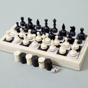 Könnte beinhalten: Ein komplettes Schachspiel mit schwarzen und weißen Figuren auf einem Schachbrett. Das Set enthält Dame-Spielsteine und zwei Würfel. Das Brett und die Figuren sind elfenbein- und schwarzfarben.