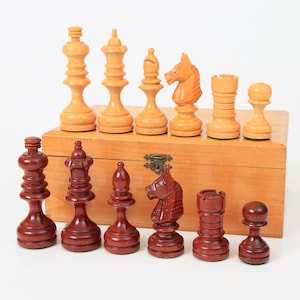 May include: A set of wooden chess pieces in a wooden box. The pieces are in two colors: brown and natural wood. The pieces are arranged in two rows, with the brown pieces in the front row and the natural wood pieces in the back row.