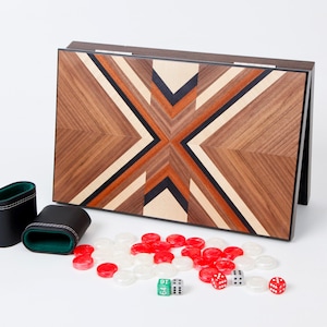 May include: A wooden backgammon set with a geometric design in shades of brown, beige, black, and orange. Includes black leather dice cups, red and white game pieces, and dice.