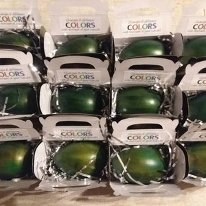 May include: Twelve small white boxes with clear lids, each containing a green egg-shaped object. The boxes have a label that reads "Changes & different COLORS with the turn of your hand!"