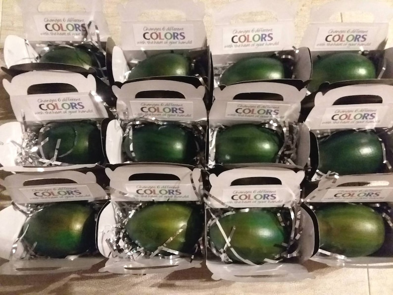 May include: Twelve small white boxes with clear lids, each containing a green egg-shaped object. The boxes have a label that reads "Changes & different COLORS with the turn of your hand!"