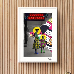 May include: Framed art print featuring a photograph of two people standing under a sign that reads "COLORED ENTRANCE." The print has a white border and is mounted on a wooden slatted wall. The photograph has a colorful, graphic design.