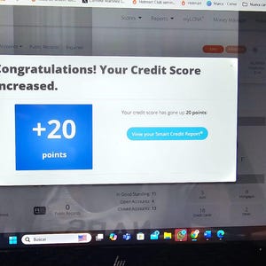 May include: A laptop screen shows a credit report with a pop-up message. The message reads "Congratulations! Your Credit Score Increased." A blue box shows "+20 points." The screen also has navigation icons and text related to credit reports.