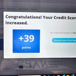 May include: A computer screen shows a pop-up message: "Congratulations! Your Credit Score Increased." A blue square displays "+39 points." The text "View your Smart Credit Report" is visible. The screen shows credit report details.