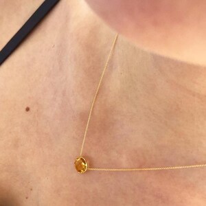 May include: A gold chain necklace with a single, round, yellow gemstone pendant.